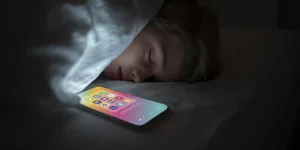 Personne utilisant son smartphone dans son lit la nuit avec lumière bleue perturbant le sommeil